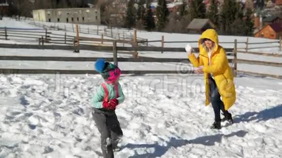 快乐的母亲正在和她的女儿户外玩雪球穿黄色外套的女人和小女孩视频的预览图