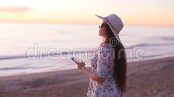戴帽子的年轻女游客在海洋海滩日落时拍照视频的预览图