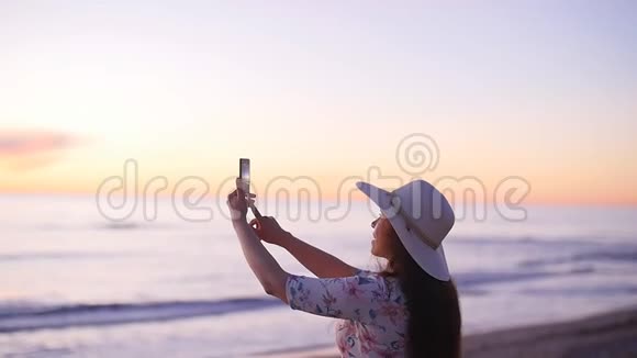 戴帽子的年轻女游客在海洋海滩日落时拍照视频的预览图