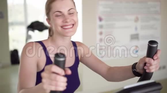 漂亮的适合年轻女子在健身房做运动的天鹅绒模拟器对着镜头微笑视频的预览图