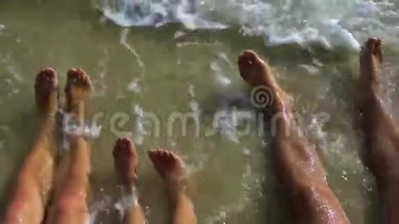 脚在海里的水里三双腿一个男人一个女人和一个男孩坐在海滩上他们的脚被海水冲刷视频的预览图