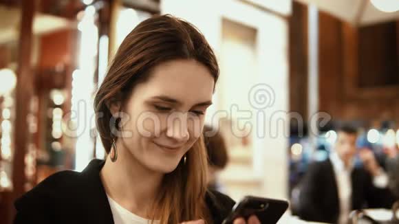 晚上坐在市中心在咖啡馆里使用智能手机的年轻美女肖像视频的预览图