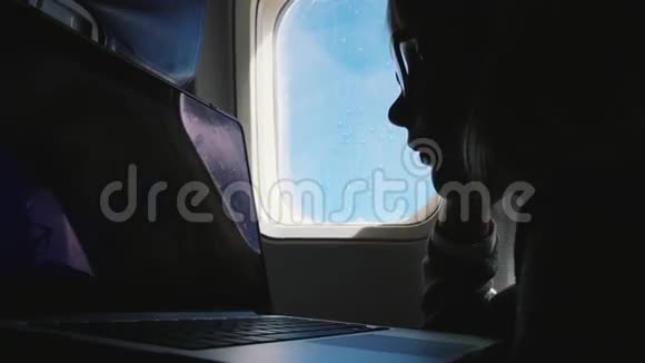 一个戴眼镜的女孩看着笔记本电脑屏幕的剪影在飞机里飞行视频的预览图