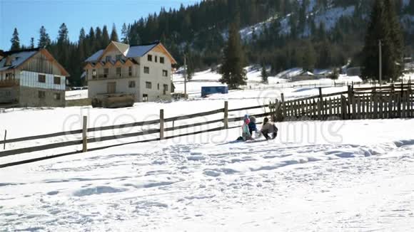 孩子们正在户外一起玩冬季游戏两个女孩和一个男孩正在山上滚一个大雪球视频的预览图