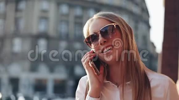 年轻的女商人站在阳光明媚的城市街道上的办公楼附近用手机交谈视频的预览图