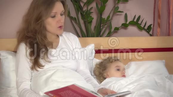 可爱的小女孩躺在床上而母亲的女人读故事书视频的预览图