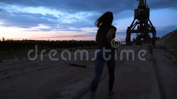一个年轻的女人穿着运动服沿着货运港的沙墩慢跑在黎明的黄昏视图视频的预览图