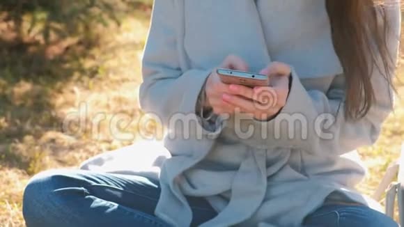 年轻漂亮的黑发女人坐在春天公园的草地上用手机输入一条信息特写双手视频的预览图