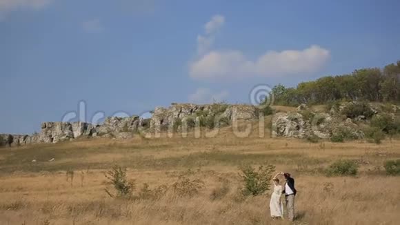 快乐的一对夫妇在草地上玩得很开心一对夫妇在岩石和蓝天的背景下跳舞视频的预览图