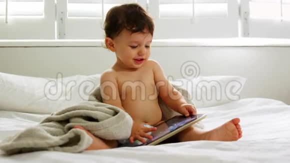 一个小男孩正在床上看他的平板电脑视频的预览图