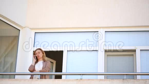 一个年轻的女人走到阳台上环顾四周她微笑着凝视着远方在电话里说话视频的预览图