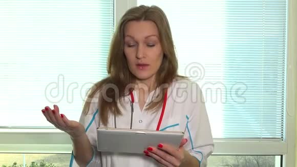 女医生带着平板电脑看着摄像机在视频会议上讲话视频的预览图