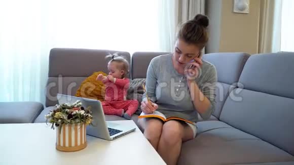 家庭幸福妈妈和宝贝一位年轻的母亲在家拿着笔记本电脑工作视频的预览图