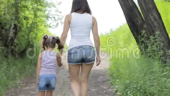 家庭价值观年轻的妈妈牵着小女孩的手在公园散步后退视频的预览图