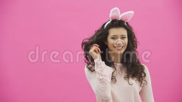 美丽的年轻女孩站在粉红色的背景上在这期间头上有兔子的耳朵视频的预览图
