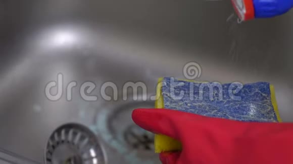 女人用红色手套在厨房里洗了一个带海绵的金属水槽双手特写视频的预览图
