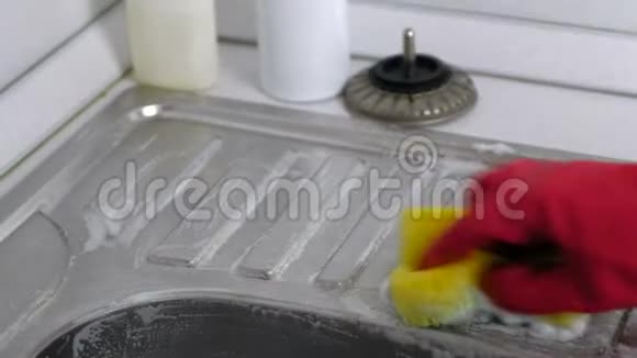 女人用红色手套在厨房里洗了一个带海绵的金属水槽双手特写视频的预览图