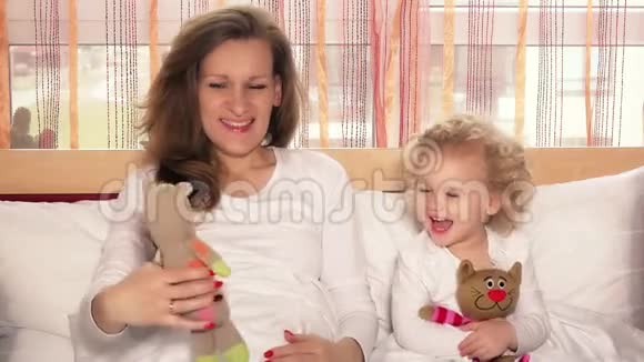快乐的微笑妈妈和她的小女孩在床上玩玩具猫视频的预览图