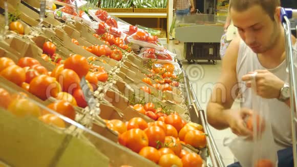 年轻人正在杂货店里选择西红柿微笑着快乐的男人选择新鲜成熟的红西红柿视频的预览图