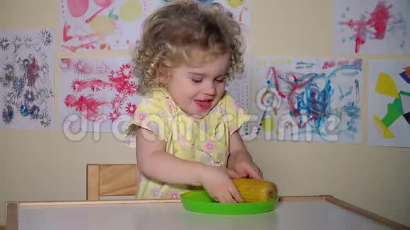 一个年轻有趣的女孩坐在家里的桌子旁吃着煮玉米视频的预览图
