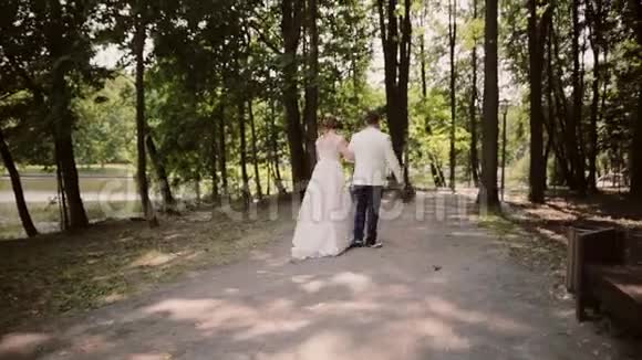 婚礼当天一对幸福的夫妇在公园的河岸上牵手散步漂亮的白色衣服视频的预览图