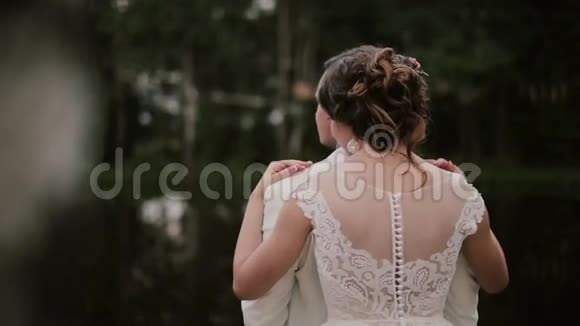 恋人们和平地站在一起新娘拥抱站在他身后的新郎穿着漂亮白色裙子的女人背面视频的预览图