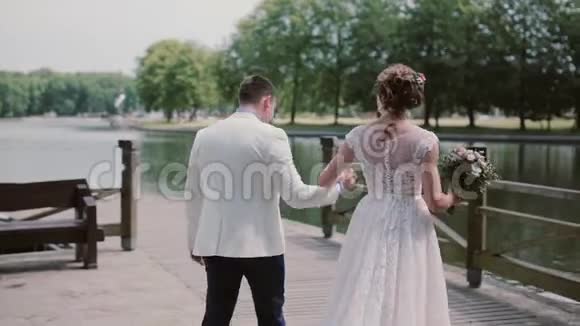 很棒的一对夫妇穿着结婚礼服走在码头上他们牵手聊天玩得开心美丽的大自然背面视频的预览图
