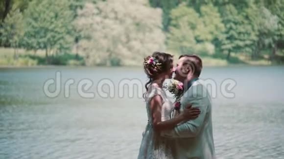 婚礼当天亲吻情侣的侧景幸福的新娘和新郎在河岸上一个美丽的地方笑视频的预览图