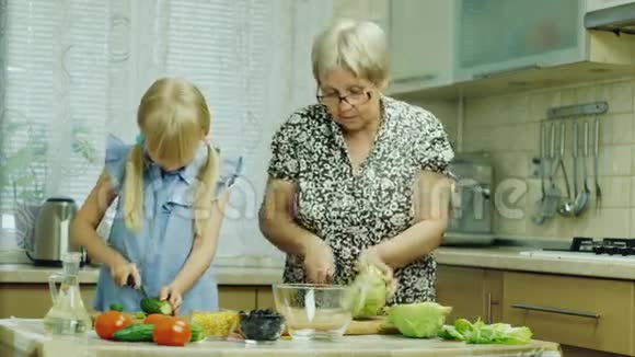 奶奶和孙女在厨房准备沙拉玩得开心笑女孩帮奶奶视频的预览图