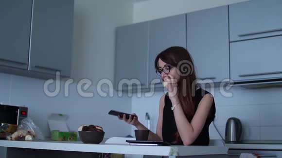 有魅力的年轻女性使用智能手机在厨房吃饭视频的预览图