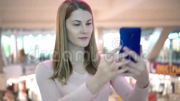 漂亮的女人穿着一件粉红色的衬衫在商场里有一部智能手机做自拍微笑玩得开心视频的预览图