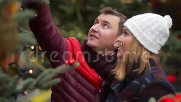 快乐夫妻在圣诞集市上选择圣诞树年轻的家庭在圣诞集市上聊天和接吻祝你快乐视频的预览图
