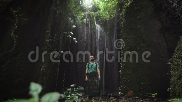 一位时尚的男性探险家在他身后瀑布附近的洞穴里休息站在海湾里的年轻人视频的预览图
