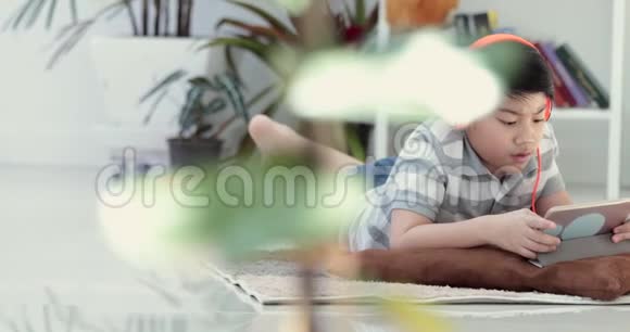 亚洲青少年前休息在地板上玩平板电脑与微笑的脸在家里视频的预览图