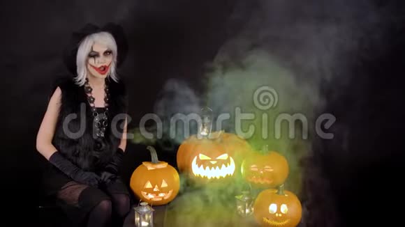 可怕的美丽女孩女巫庆祝万圣节与有趣的发光南瓜在烟雾中灰色女巫师视频的预览图