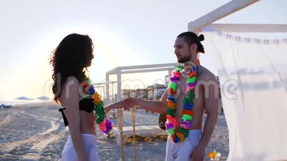 在海滩上的情侣们在异国情调的度假胜地的情侣们慢舞男人牵着女孩的手把她腰带到海滩上视频的预览图