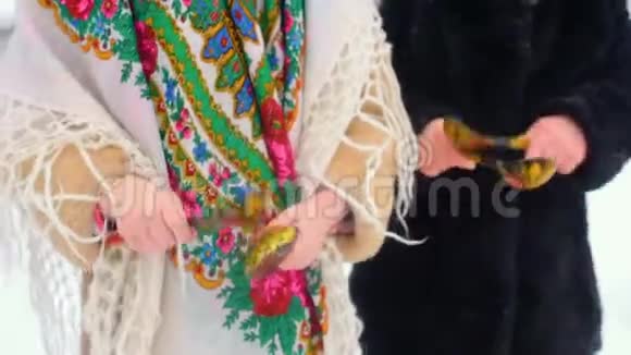 两个穿着俄罗斯风格的衣服和头巾的小女孩在雪地里用木勺玩视频的预览图