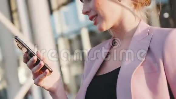 一位年轻的金发商务女士在灿烂的阳光下微笑着使用她的手机现代技术视频的预览图