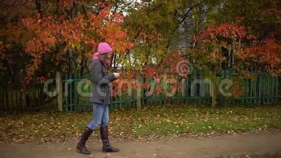 年轻漂亮的女人用她的手机在黄叶背景下在手机上写信息而视频的预览图