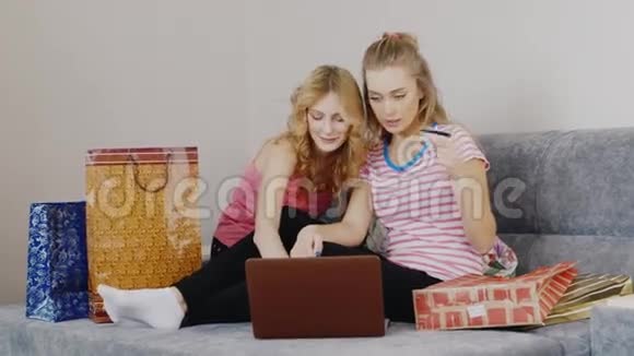 两个年轻的女人在网上买东西坐在卧室的床上谈论他们的购物袋和笔记本电脑视频的预览图