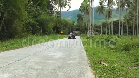 男子骑自行车沿着棕榈树林的道路行驶视频的预览图