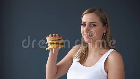 超重的女人在灰色背景下吃汉堡包有害食物超重的概念视频的预览图