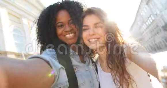 美丽的微笑的多元文化女孩的情感自拍在街上散步时做滑稽的脸视频的预览图