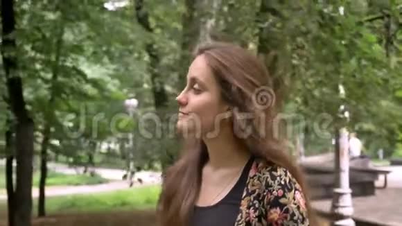 一位留着长发的年轻美女她带着绿树漫步在公园里微笑着开心快乐视频的预览图