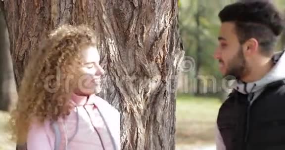 年轻夫妇站在树旁说着英俊的男人和漂亮的女人户外晨曦秋园视频的预览图