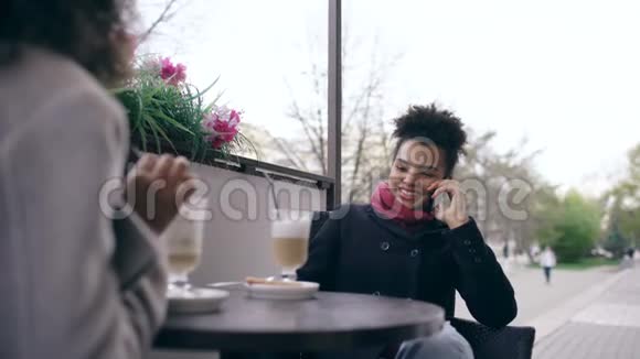 两个混血女人坐在街头咖啡馆的桌子旁用智能手机说话视频的预览图