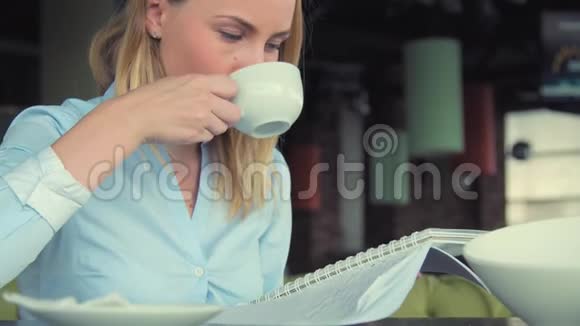 现代女孩在咖啡馆喝茶使用平板电脑和写在笔记本在咖啡店工作的漂亮女孩视频的预览图
