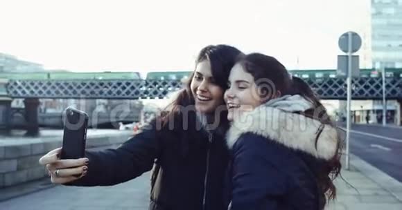 两个年轻漂亮的长发女孩坐在火车桥前用智能手机自拍射入视频的预览图
