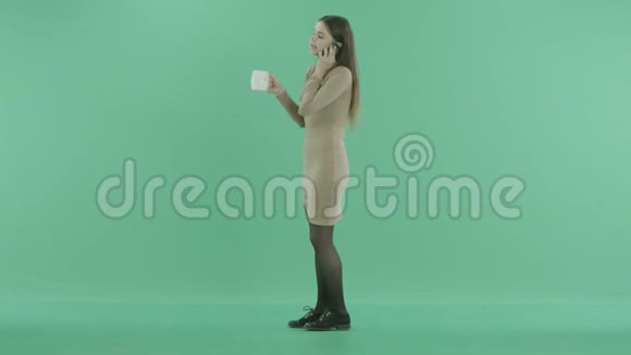 女人拿着一杯茶站在电话里视频的预览图