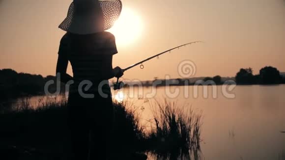 戴着帽子的年轻女人的剪影在黎明时分用鱼竿捕鱼视频的预览图